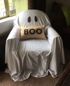 a white chair with a boo pillow on it's back in front of a window