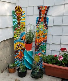 some plants are sitting in pots on the side of a building with decorative art behind them