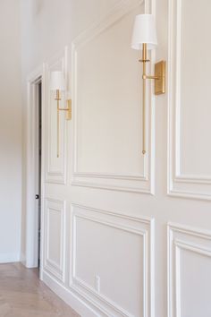 an empty room with white walls and gold trim on the wall, along with two lamps