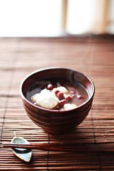 a wooden bowl filled with food on top of a bamboo table next to a spoon