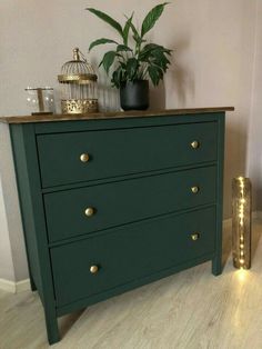 a green dresser with gold handles and drawers next to a potted plant on top