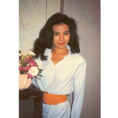 a woman standing in front of a mirror holding a bouquet of flowers and wearing a white shirt