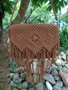 a crocheted bag hanging from a tree in front of some rocks and trees