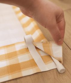 a person is cutting fabric with scissors on a wooden tablecloth that has yellow and white checkered material