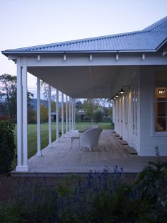 an outdoor covered patio with chairs and tables on the deck at dusk, in front of a white house