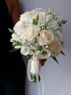 a bridal bouquet with white roses and baby's breath in someones hand