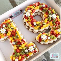 a number shaped cake on top of a white box with flowers and leaves in it