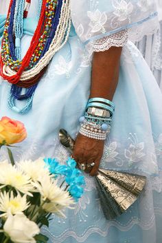 a close up of a person wearing beads and bracelets with flowers in the background