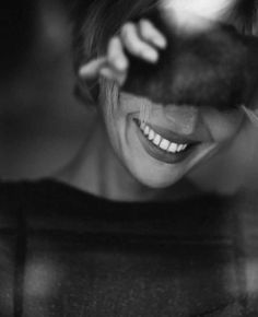 black and white photograph of smiling woman with cat's paw in her mouth, taken from behind