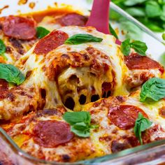 a casserole dish with pepperoni, cheese and spinach leaves on top