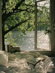 an open book sitting on top of a bed under a tree next to a window