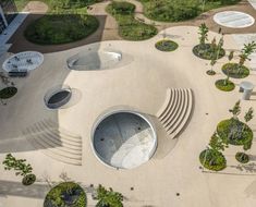 an aerial view of a circular building with trees and bushes in the foreground, surrounded by concrete steps