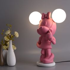 a pink pig lamp sitting next to two vases with flowers in front of it