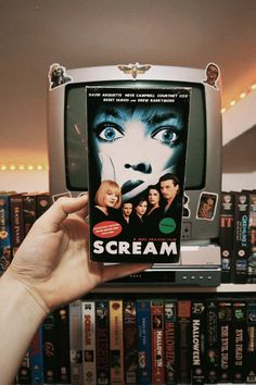 a hand holding up a dvd in front of a television screen with scream on it