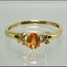 a yellow gold ring with an orange stone and three diamonds on the band, sitting on a white surface