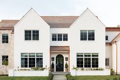 a large white house with lots of windows and plants on the front lawn in front of it