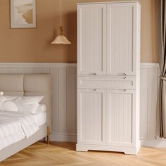 a white bed sitting next to a tall cabinet in a bedroom on top of a hard wood floor