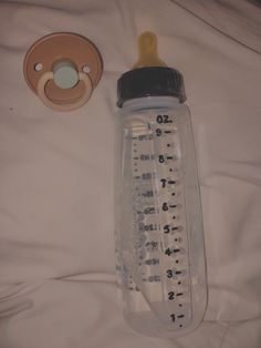 a baby bottle with a thermometer next to it on a white bed sheet