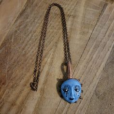 a necklace with a face on it sitting on a wooden floor next to a chain