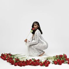 a woman sitting on the ground with roses in front of her and holding a rose