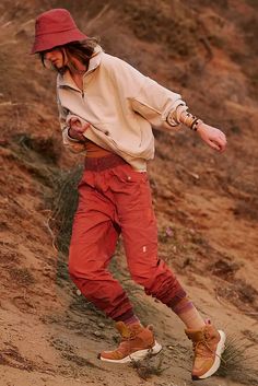 a man wearing red pants and a hat is walking on the sand with his foot in the air