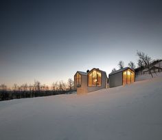 two small houses sitting on top of a snow covered hill next to each other in the evening