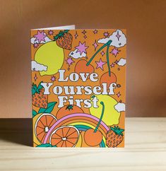 an orange card with the words love yourself first written in white on it, surrounded by fruit and clouds