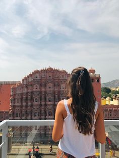 a woman standing on top of a balcony next to a tall building with lots of windows