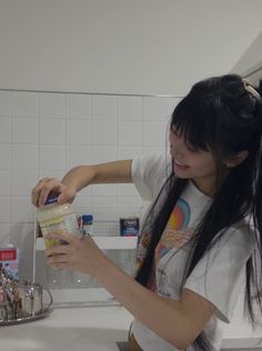 a woman is washing her long hair in the bathroom sink while holding a container with some liquid on it