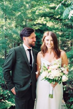 a bride and groom standing on a bridge in the woods smiling at each other as they pose for a photo