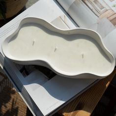 a book is open on top of a table with a white vase in the shape of a wave