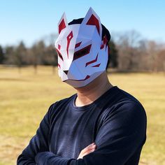 a man wearing a paper mask with his arms crossed in front of him, standing in a field