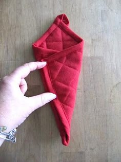 a hand is holding a red towel on a wooden table next to an object that appears to be folded up