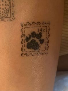 a dog paw tattoo on the back of a woman's leg, with a postage stamp behind it