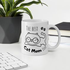 a white coffee mug sitting on top of a desk next to a keyboard and plant