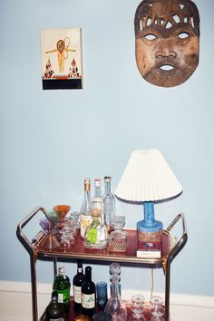 a bar cart with liquor bottles and glasses on it in front of a blue wall