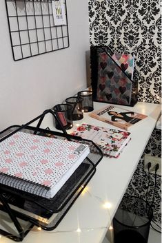 a white desk topped with lots of papers and binders next to a wall covered in black and white damask