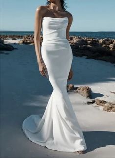 a woman in a white wedding dress standing on the beach with her hand on her hip