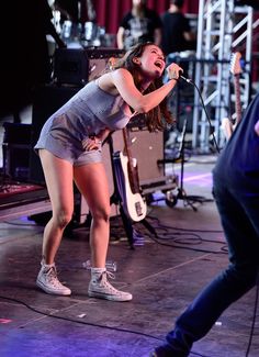 a woman singing into a microphone while standing next to another person on stage with other people in the background