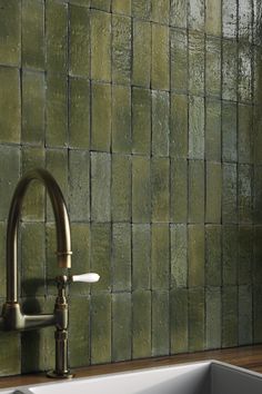 a white sink sitting under a faucet next to a green tile backsplash