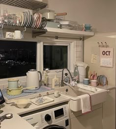 a kitchen filled with dishes and appliances next to a window overlooking the city at night