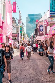 many people are walking down the street in front of shops and buildings with pink signs