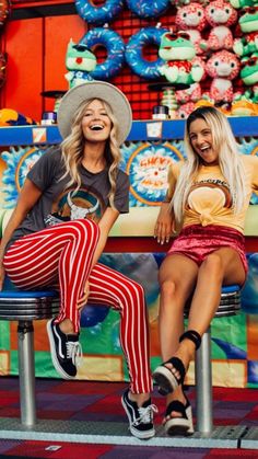 two women are sitting on stools in front of a carnival booth and smiling at the camera