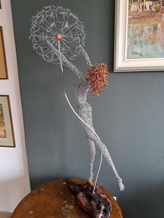 a wire sculpture holding an umbrella on top of a wooden table next to a painting