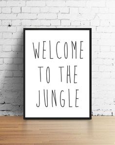 a black and white sign that reads welcome to the jungle on a wooden table in front of a brick wall