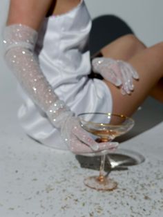 a woman sitting on the floor next to a glass filled with liquid and wearing white gloves