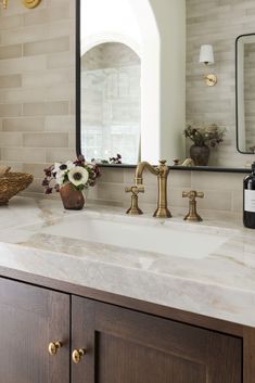 a bathroom sink with marble counter top and gold faucet, along with a bottle of wine