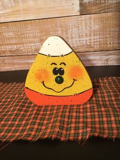 an orange and white painted rock sitting on top of a checkered table cloth next to a wooden wall