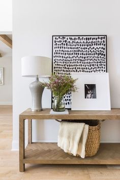 a wooden table topped with a vase filled with flowers next to a lamp and pictures on the wall