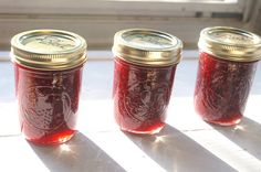 three jars filled with red liquid sitting on top of a white table next to a window